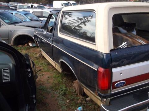 1994 Ford Bronco - The rear driver's side quarter of a dark blue and tan 1990s Ford Bronco is shown parked in a grassy lot with other vehicles. A sticker read…