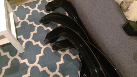 1994 Ford Bronco - Several black exhaust headers are laid out on a blue and white patterned rug next to a grey upholstered couch. A portion of a white table l…