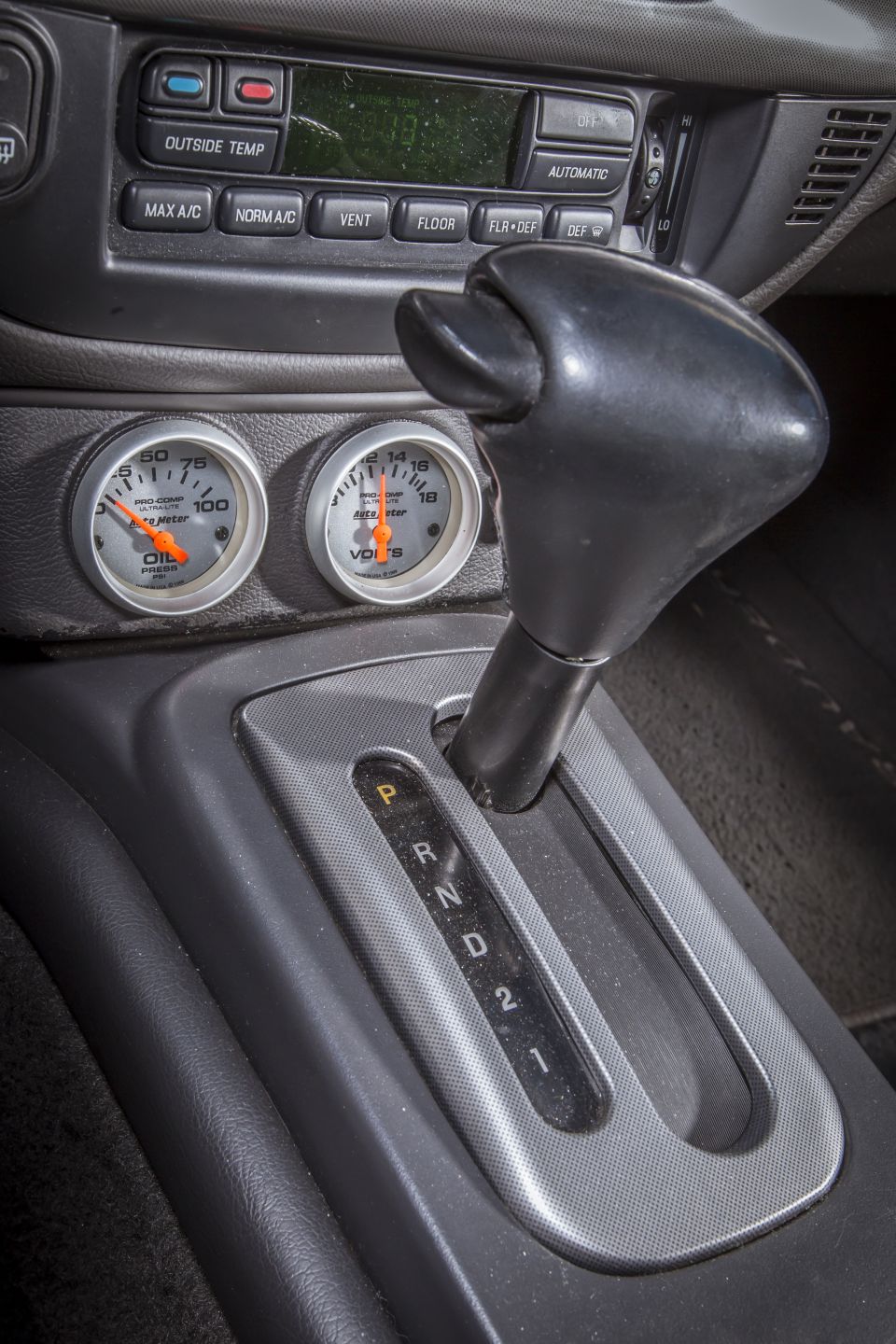 Close-up of car interior: automatic gear shifter, oil pressure gauge, and voltmeter.