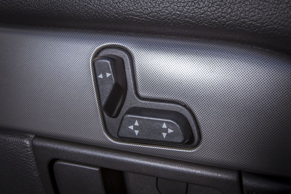 Close-up of black power seat controls with directional arrows on a car door panel.