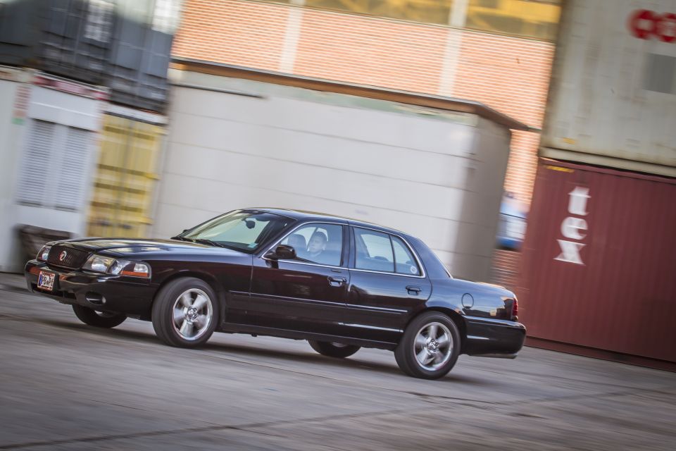 Black 2003 Mercury Marauder driving, 3/4 front view, with shipping containers in background.