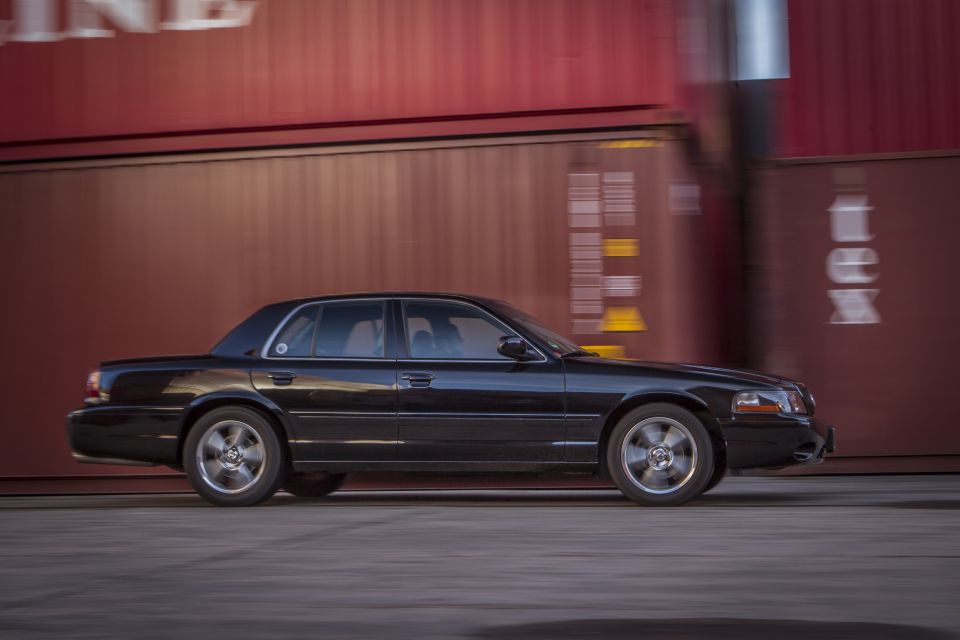 Black 2003 Mercury Marauder in motion, side view, passing blurred red shipping containers.