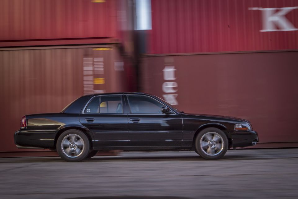 Black sedan in motion next to blurred red shipping containers.