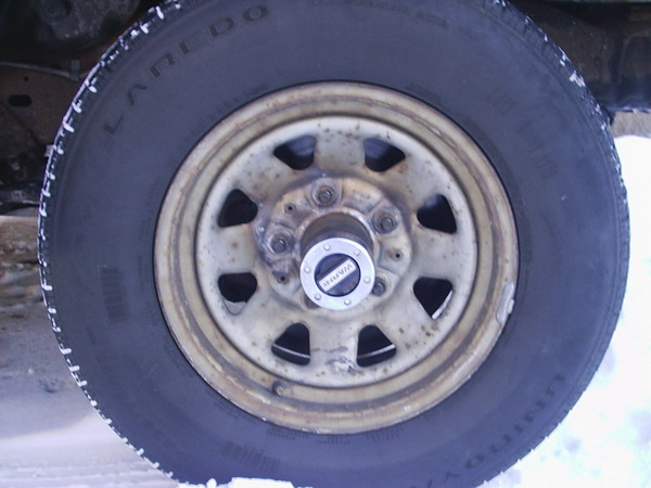 Close-up of Laredo tire on dirty white steel wheel with manual locking hub, snow visible below