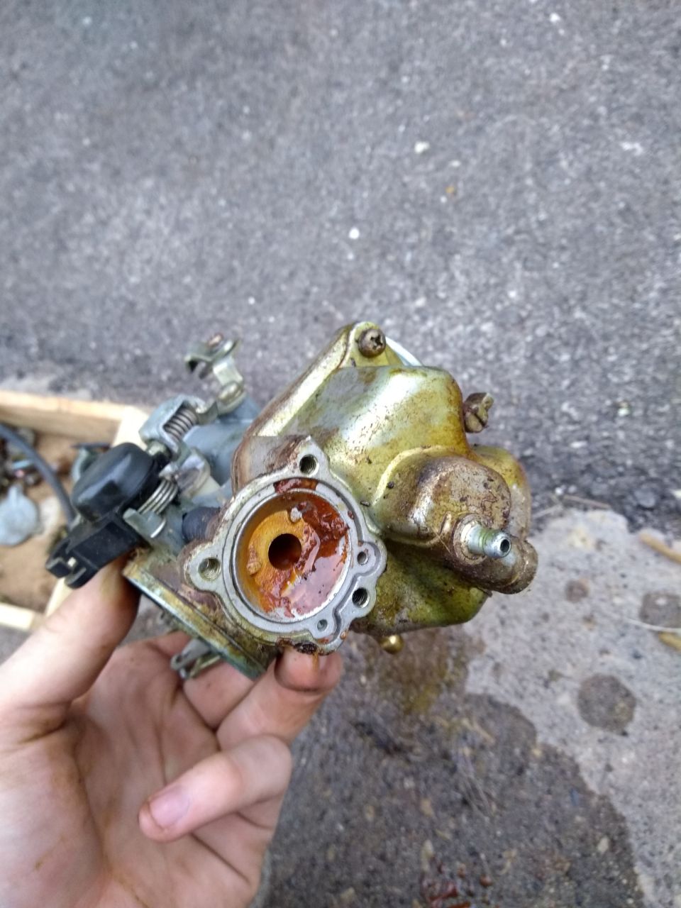 Close-up of a dirty, rusty motorcycle carburetor held in a hand.