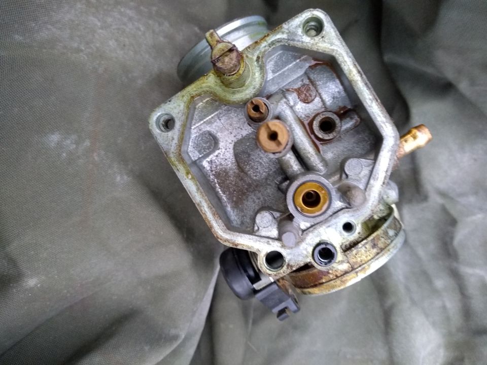 Disassembled motorcycle carburetor on olive green fabric