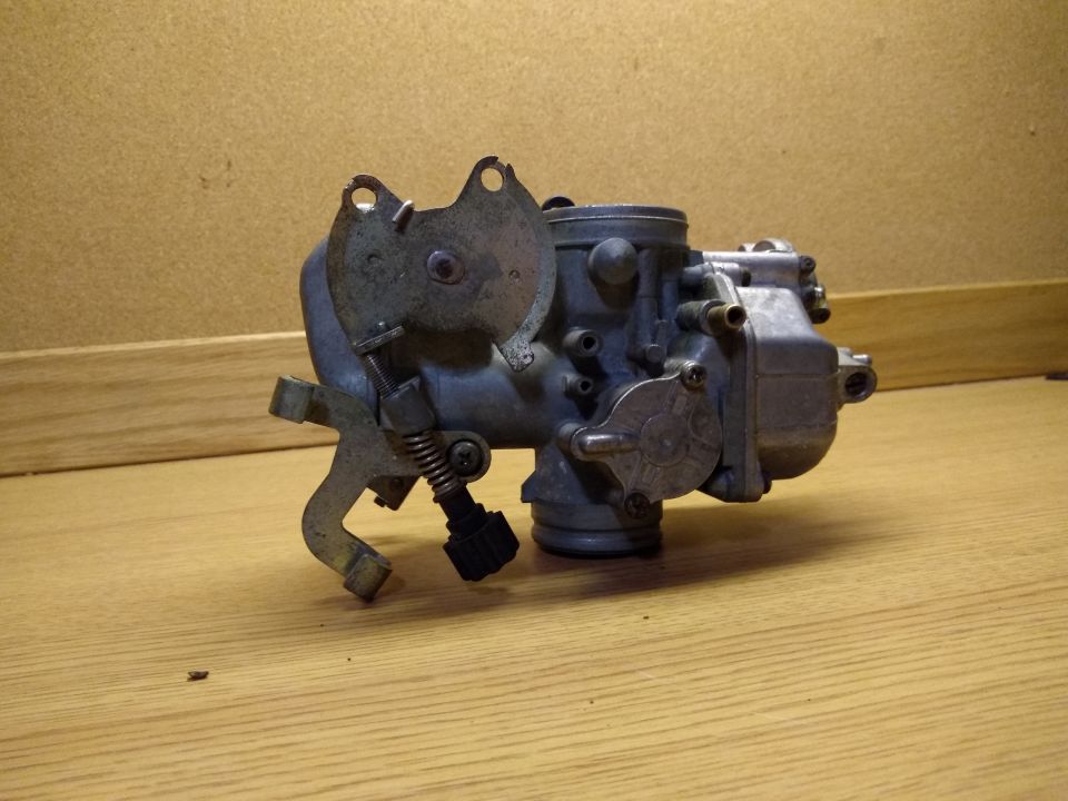 Motorcycle carburetor on a wooden table.