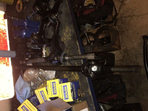 1995 Ford F-150 - A collection of automotive parts, including axle shafts, differential gears, and steering components, are laid out on a workbench.