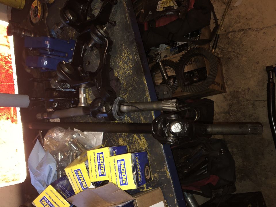 Automotive parts including axle shafts, differential gears, and steering components on a workbench.
