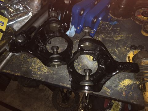 1995 Ford F-150 - Two black painted suspension steering knuckles with ball joints are laid out on a worn workbench next to other automotive parts.