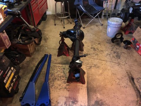 1995 Ford F-150 - A black painted rear axle assembly is supported by red jack stands on a concrete floor. Various automotive parts and tools are scattered ar…