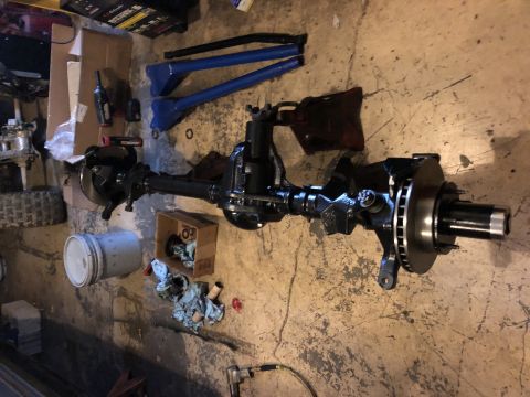 1995 Ford F-150 - A black front axle assembly with disc brakes is laid out on a concrete floor, possibly in a garage or workshop. Various tools and parts are…