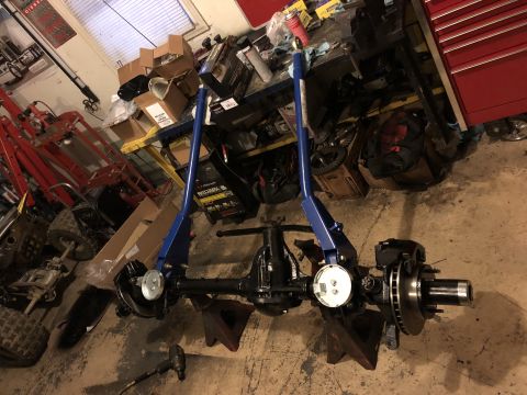 1995 Ford F-150 - A black Ford F-150 rear axle assembly is mounted on jack stands in a garage. The axle features disc brakes and a dial indicator is attached…