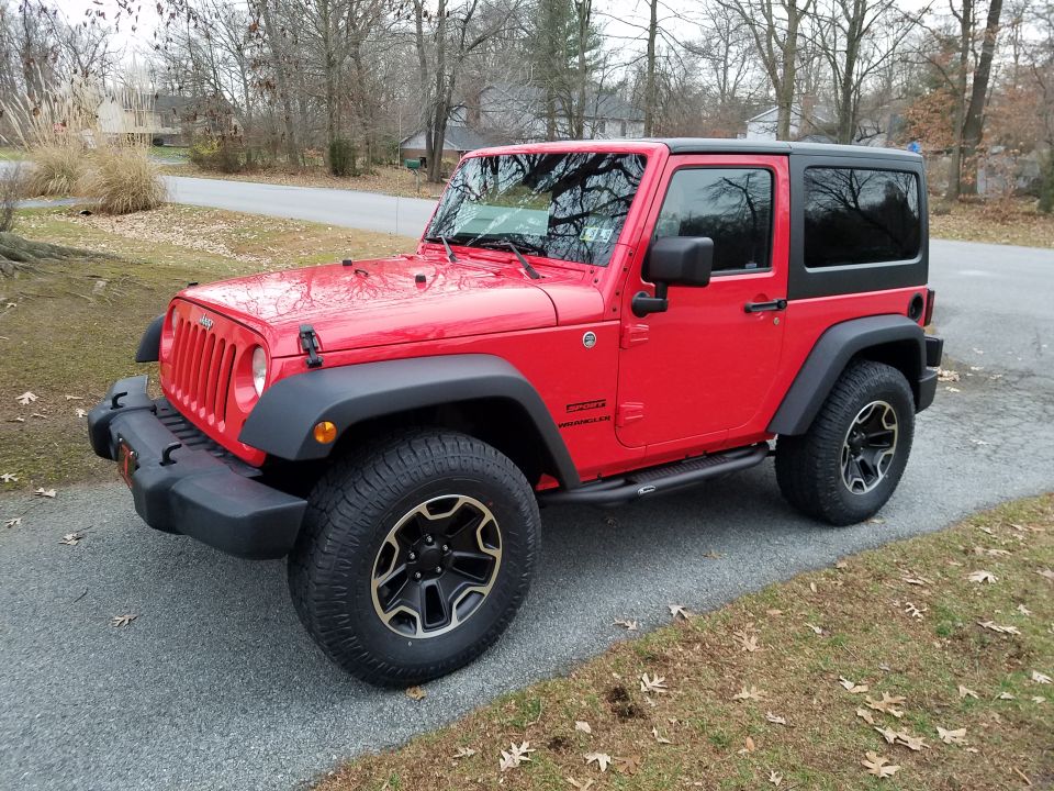 Red two-door Jeep Wrangler parked on a gravel driveway.