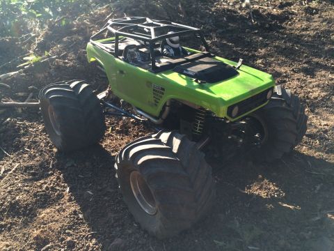 1989 Ford Bronco - A bright green RC rock crawler with oversized tires is positioned on a dirt terrain, with a roll cage visible over the cabin.