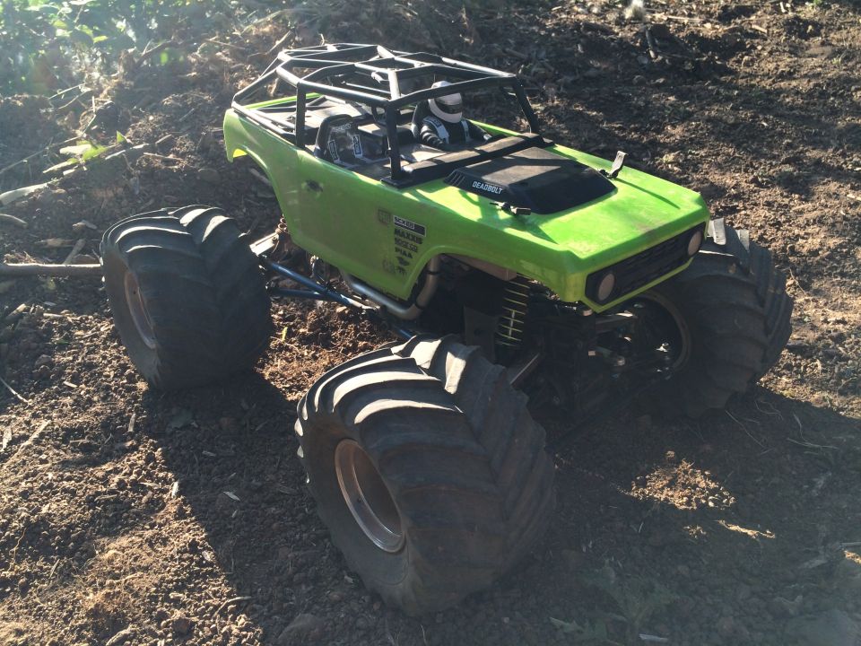 Green RC rock crawler with large tires and roll cage on dirt.