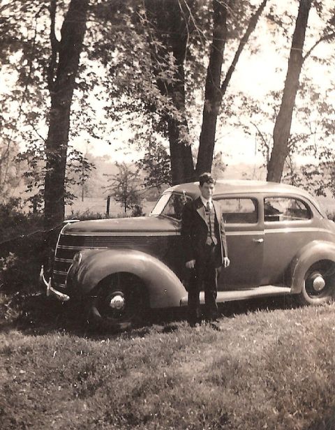 1967 Ford Custom Wagon - A man in a suit stands next to a vintage sedan parked on a grassy area with trees in the background.