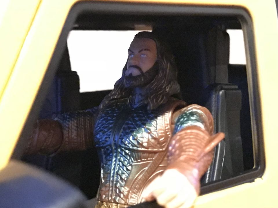 Aquaman toy figure in the driver's seat of a yellow vehicle.
