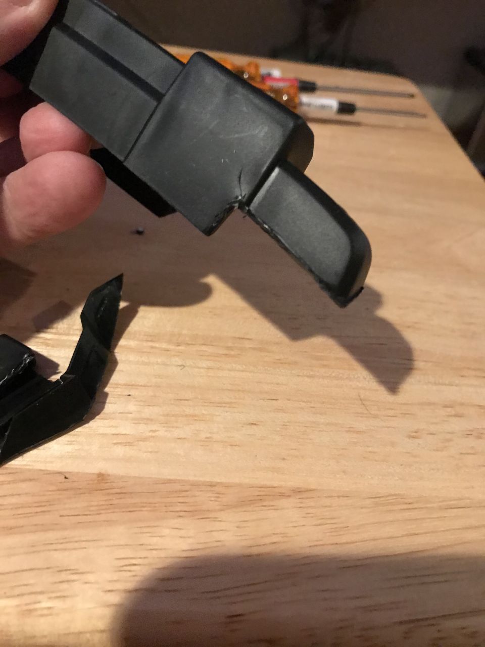 Broken black plastic part held by a hand over a wooden table.