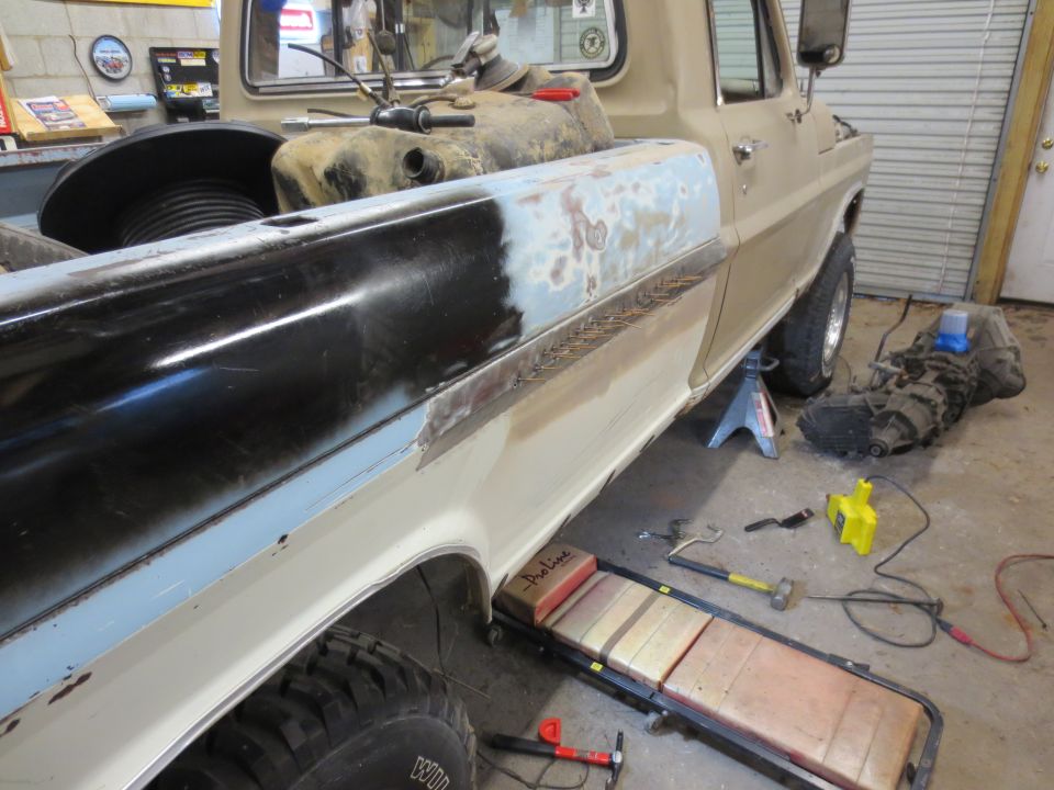 Pickup truck bed in repair, with tools and transmission on the floor.