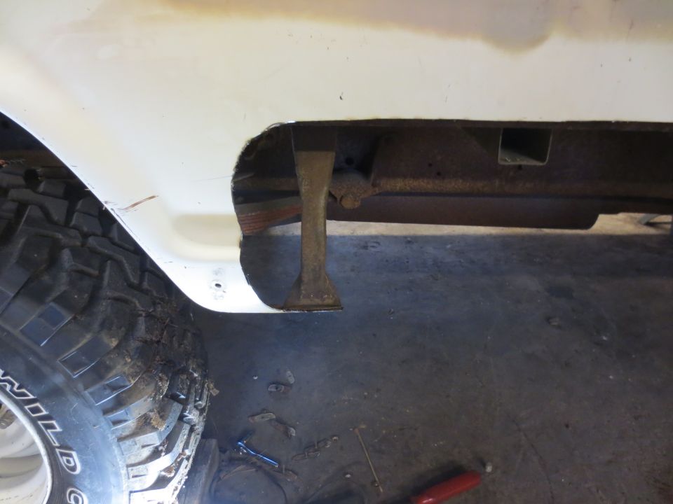 Underside of a white pickup truck fender with a cut-out, showing rusty frame and off-road tire.