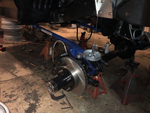 1995 Ford F-150 - A close-up view of the front suspension and braking system of a vehicle being worked on, supported by jack stands. The image shows a blue s…