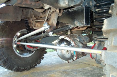 1995 Ford Bronco - Underside view of a lifted solid front axle showing a chrome differential cover, coil springs, and aftermarket adjustable tie rod and drag…