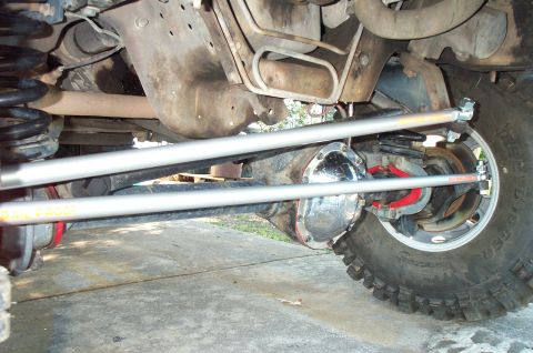 1995 Ford Bronco - Low underbody view of a lifted 4x4 front axle showing a solid axle with chrome differential cover, red radius-arm brackets and coil springs…