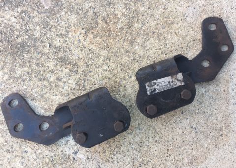1994 Ford Bronco - Two black metal brackets with bolts are shown lying on a concrete surface. One bracket has a white label with black text that reads "Servic…