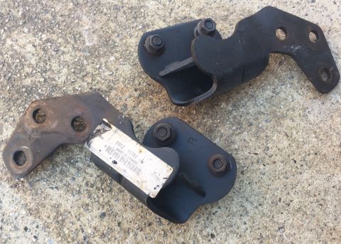 1994 Ford Bronco - Two black metal brackets are shown lying on a concrete surface. One bracket has a white label with text and a barcode attached.