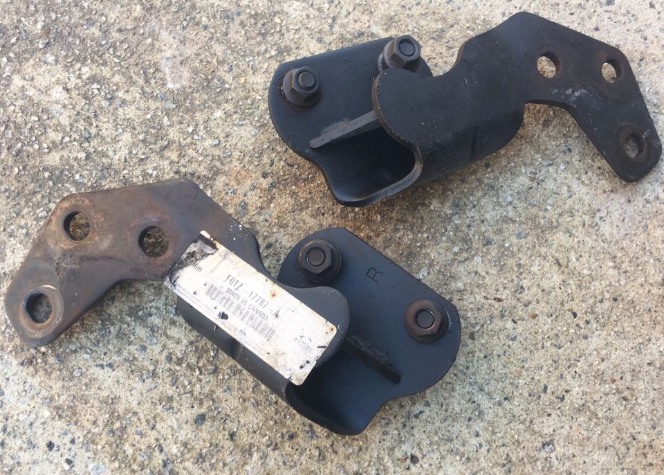 Two black metal brackets on concrete, one with a label.