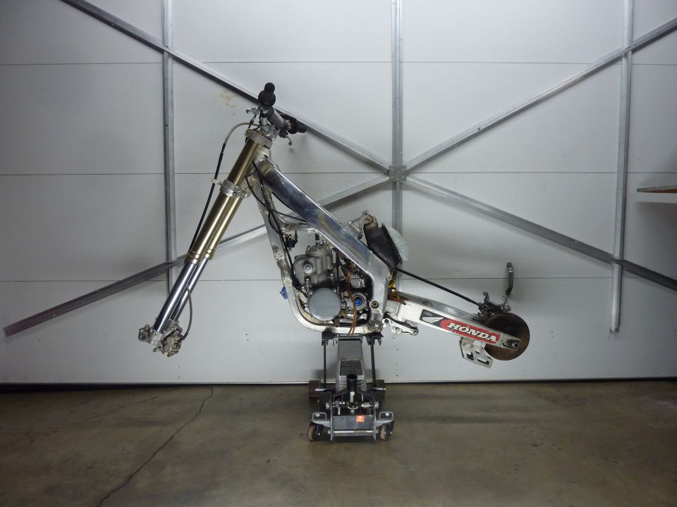 Dirt bike frame and engine on a lift with Honda logo visible.