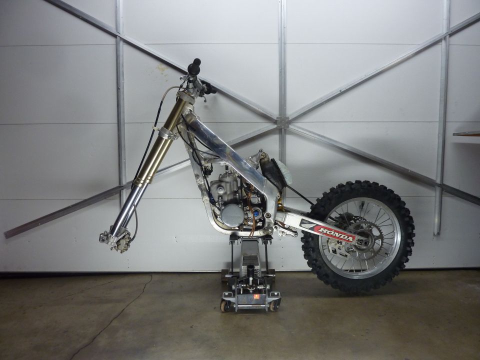 Dirt bike frame on jack stand, front forks, rear wheel with Honda sticker