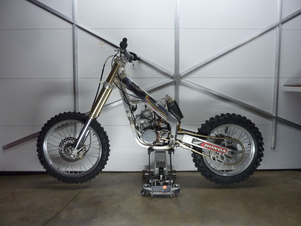 Dirt motorcycle frame with wheels, engine, and chain, on a stand.