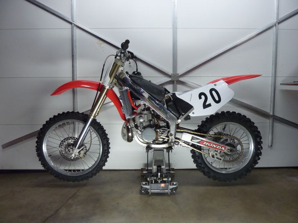 Red and white Honda dirt bike with number 20 on rear fender, elevated on a stand.