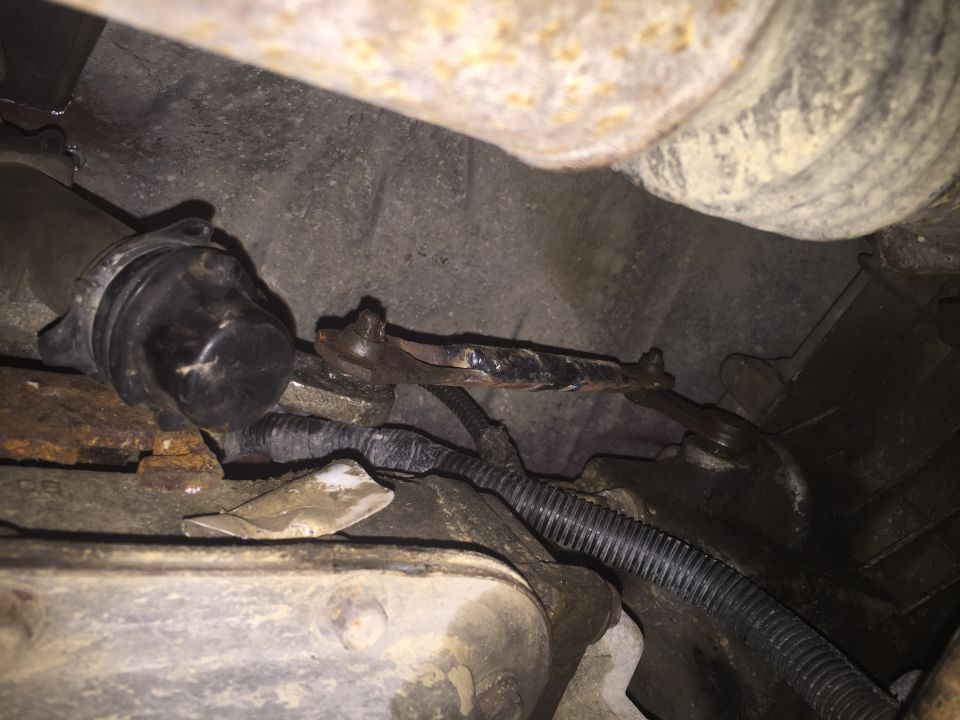 Rusted linkage and black boot on a vehicle undercarriage.