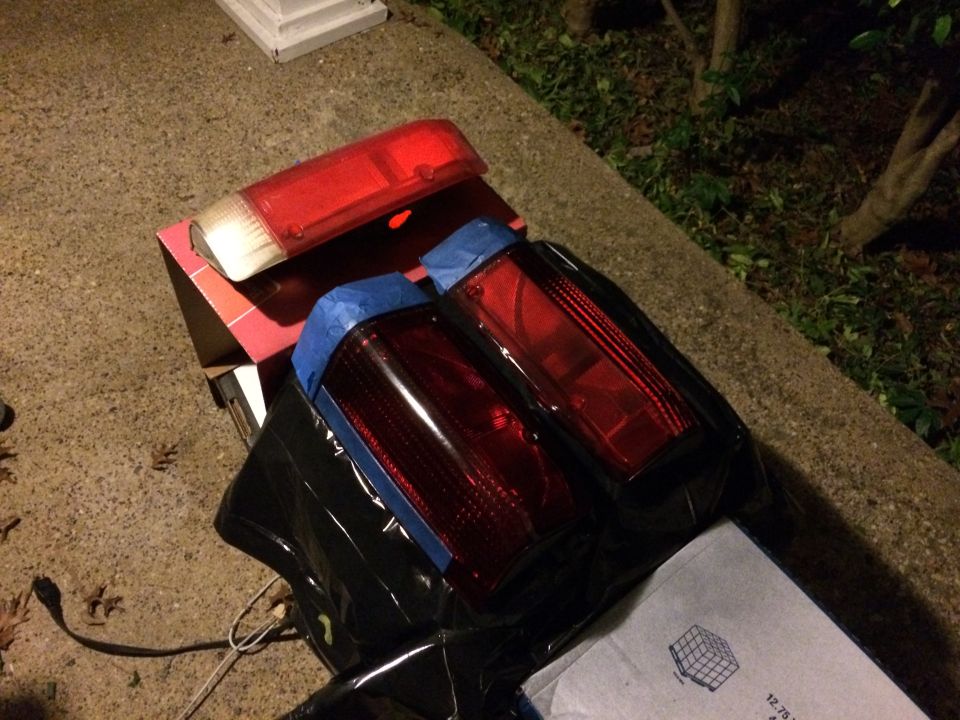 Two car taillights, one with blue tape, on a box on concrete.