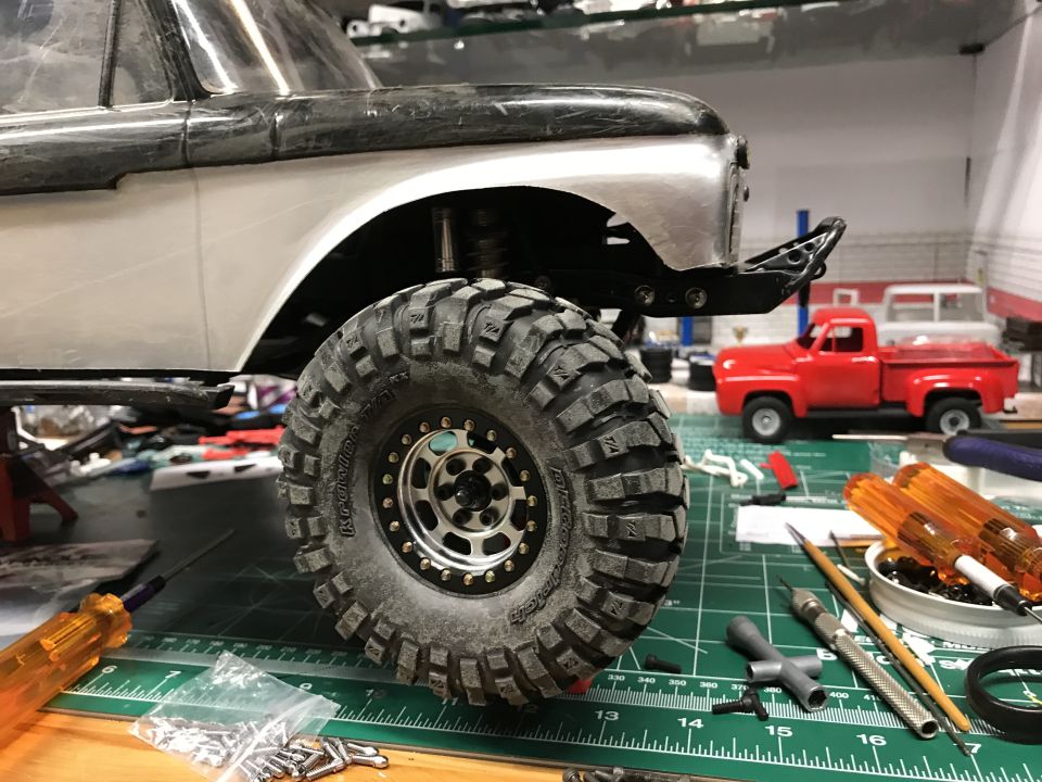 RC truck body with large tire, tools, and parts on a green mat.