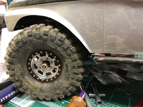 1989 Ford Bronco - Close-up of a large RC crawler tire and part of its body, with tools visible on a cutting mat.
