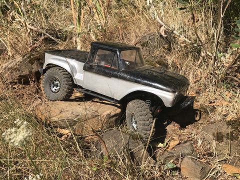 1989 Ford Bronco - This remote-controlled truck is navigating a rocky, outdoor terrain with dry grass and brush.