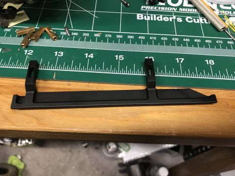 1989 Ford Bronco - A black metal bracket with mounting holes rests on a wooden surface next to a cutting mat.