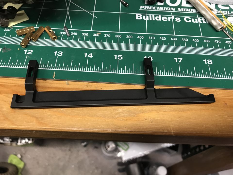 Black metal bracket with mounting holes on a green cutting mat with ruler markings