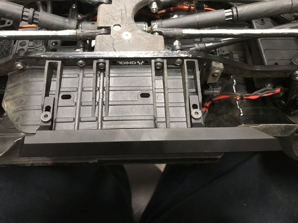 Underside of an RC car chassis with suspension components and wiring visible. Text 'AXIOL' is visible on a part