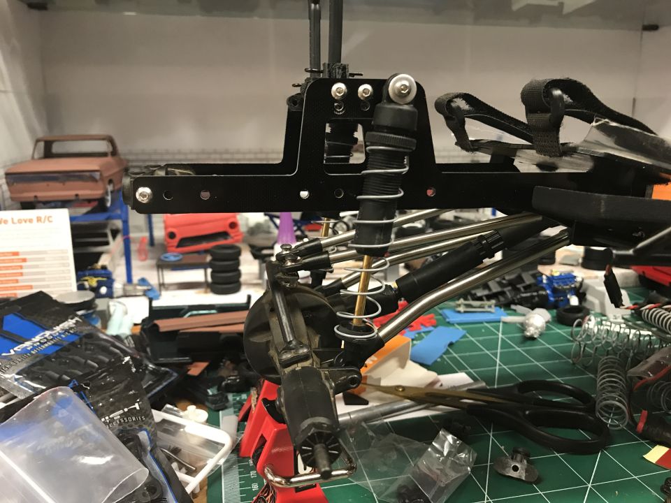 RC car suspension parts and chassis on a workbench with tools and other model car parts