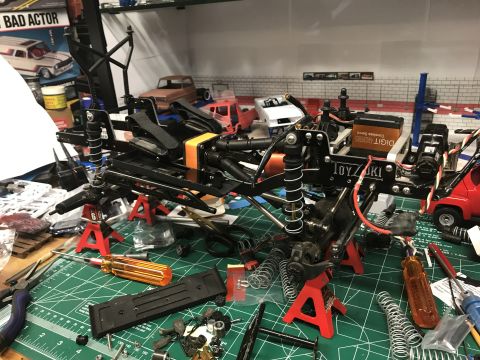 1989 Ford Bronco - RC car chassis assembly on a workbench with various tools and spare parts scattered around.