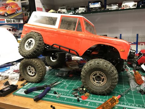 1989 Ford Bronco - This is an RC car body, likely a Ford Bronco, sitting on a workbench surrounded by tools and parts, suggesting it is a model being assemble…