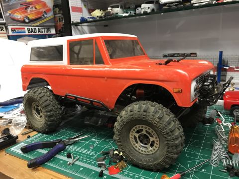 1989 Ford Bronco - An orange RC Bronco body sits on a cutting mat surrounded by tools and model car parts.