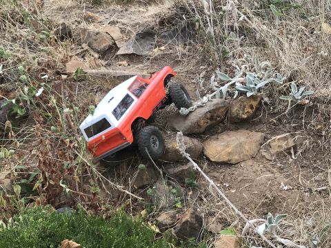 1989 Ford Bronco - An orange and white remote-controlled truck navigates a rocky, uneven terrain.