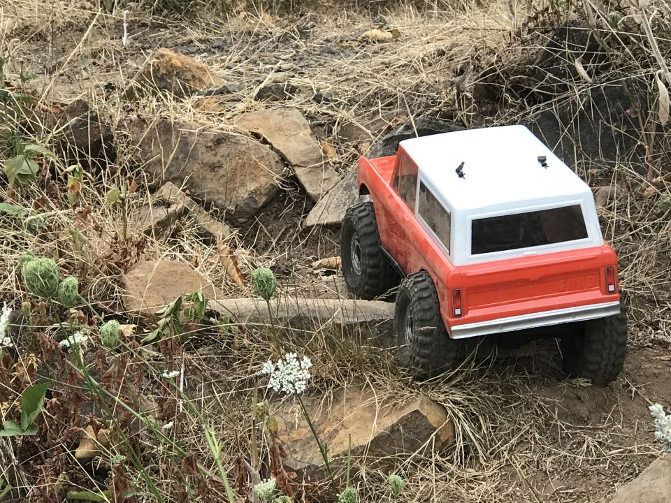 Orange and white RC Bronco rear view climbing rocky terrain