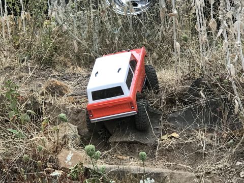 1989 Ford Bronco - A remote-controlled car with a red body and white top navigates a rough, rocky path.